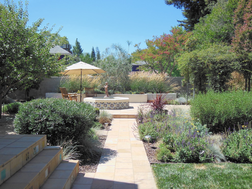 Exempel på en stor medelhavsstil trädgård i full sol på våren, med naturstensplattor och en fontän