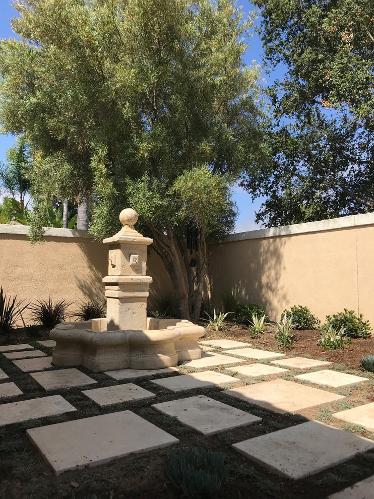 Geometrischer, Großer, Halbschattiger Mediterraner Garten im Sommer, hinter dem Haus mit Wasserspiel und Natursteinplatten in Orange County