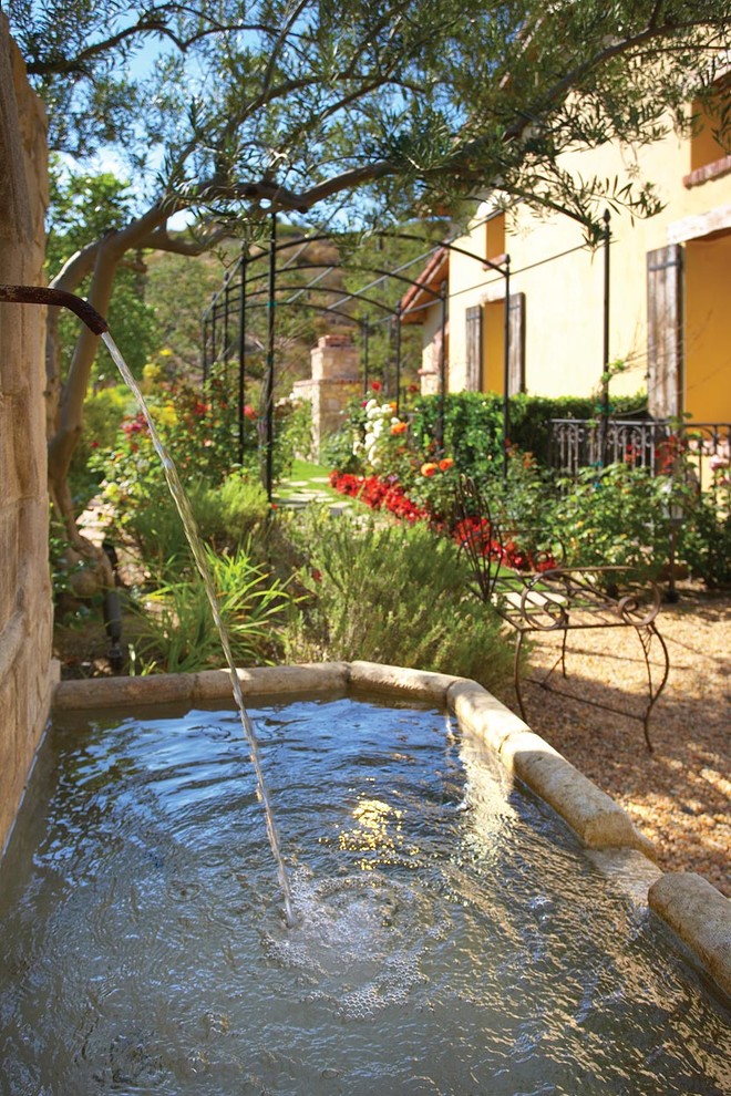 This is an example of a mediterranean side partial sun garden for spring in Orange County with a water feature and gravel.