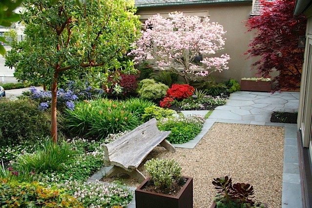 Cette image montre un jardin avant traditionnel au printemps avec un massif de fleurs, une exposition partiellement ombragée et un gravier de granite.