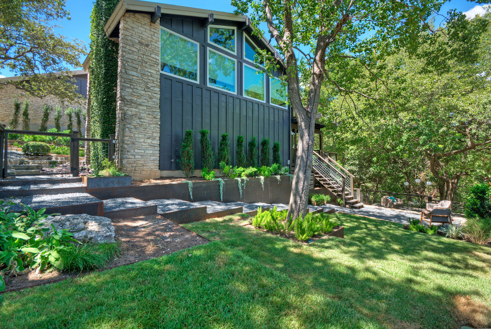 Photo of a large contemporary front xeriscape fully shaded garden for spring in Austin with a retaining wall and gravel.