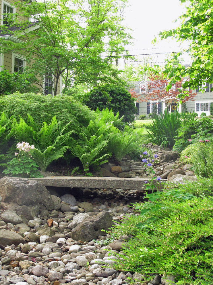 Large rustic sloped fully shaded garden in New York with natural stone paving and a garden path.