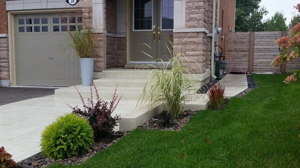 This is an example of a contemporary front driveway garden in Toronto with a retaining wall and concrete paving.