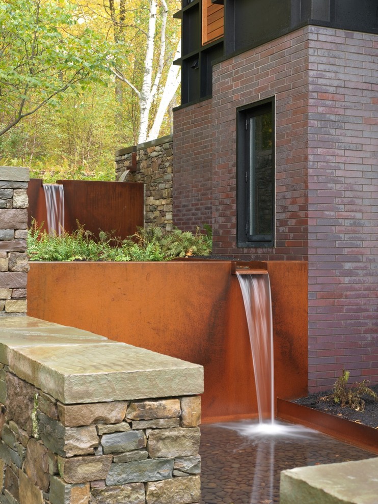 Imagen de jardín contemporáneo de tamaño medio en patio trasero con fuente, exposición total al sol y adoquines de piedra natural