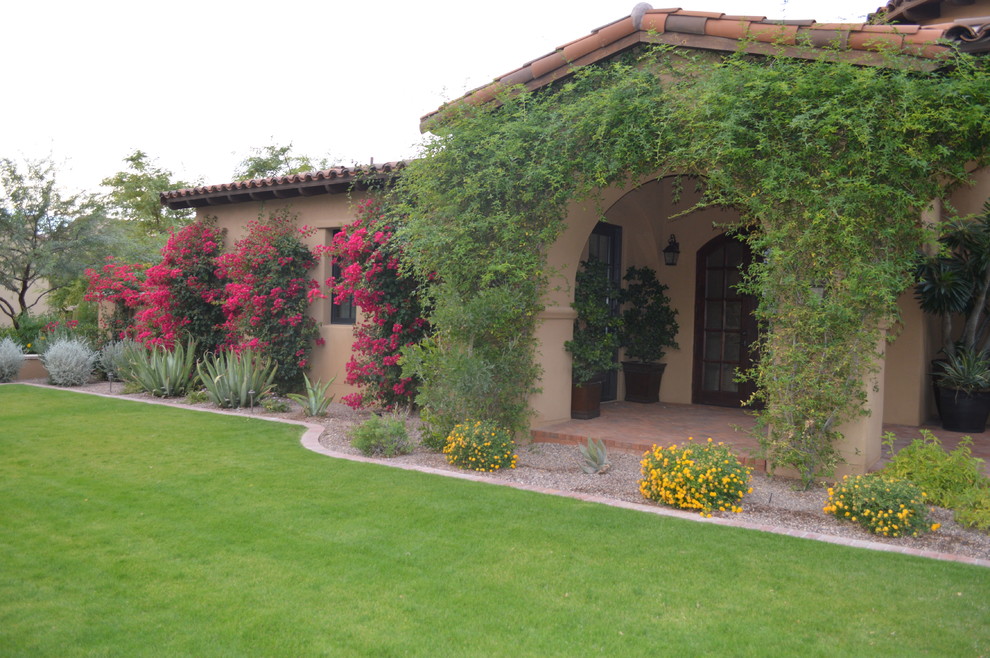Esempio di un grande giardino mediterraneo davanti casa in primavera con un muro di contenimento e pavimentazioni in mattoni