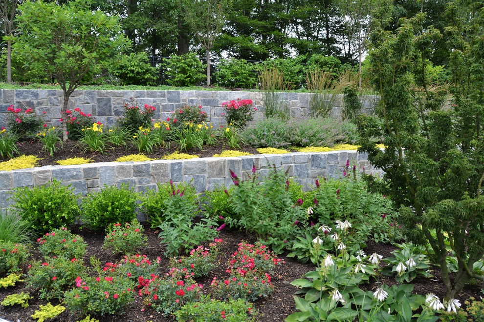 Cette photo montre un grand jardin à la française arrière moderne avec un mur de soutènement, une exposition ensoleillée et des pavés en pierre naturelle.