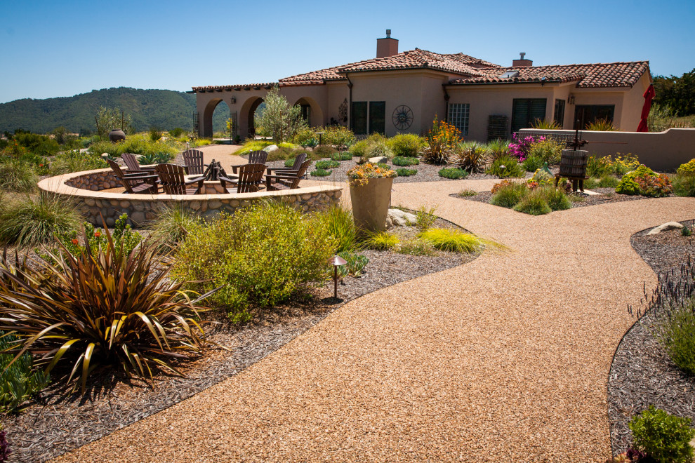 This is an example of a large mediterranean side xeriscape full sun garden for summer in San Luis Obispo with a fire feature and gravel.