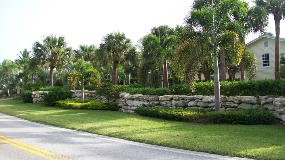 Immagine di un grande vialetto d'ingresso tropicale esposto a mezz'ombra nel cortile laterale in estate con un muro di contenimento e pavimentazioni in pietra naturale