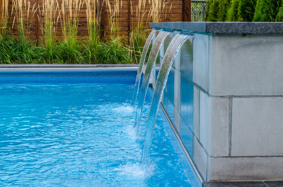 Foto de piscina con fuente actual grande en patio trasero con adoquines de piedra natural