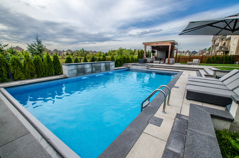 Imagen de piscina con fuente actual grande en patio trasero con adoquines de piedra natural