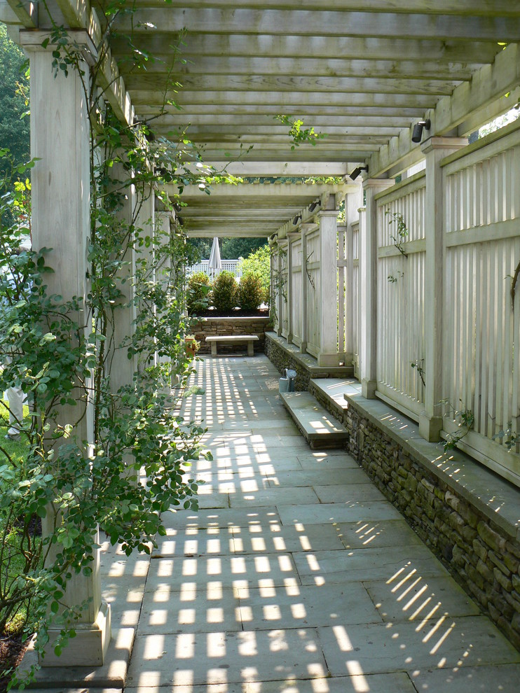 Imagen de jardín clásico grande en primavera en patio delantero con jardín francés, exposición total al sol, adoquines de hormigón, con madera y pérgola