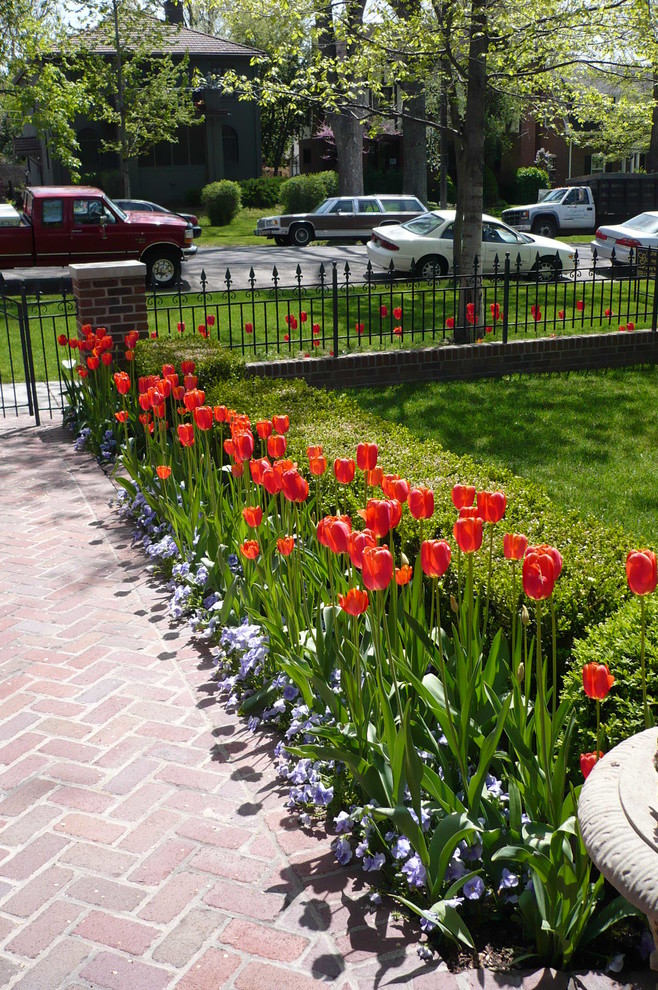 Inredning av en klassisk trädgård i delvis sol framför huset och blomsterrabatt, med marksten i tegel