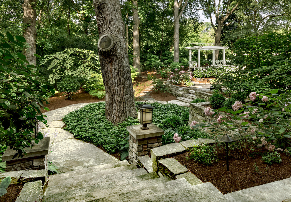 Klassisk inredning av en stor formell trädgård i skuggan framför huset, med en trädgårdsgång och naturstensplattor på sommaren