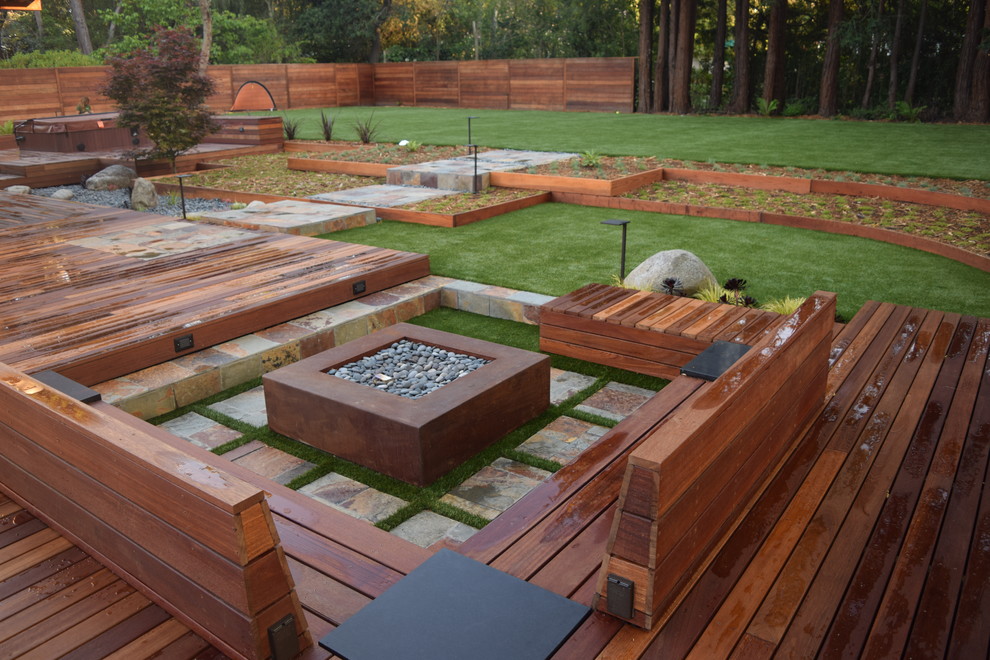Réalisation d'un grand jardin arrière design avec un foyer extérieur, une exposition partiellement ombragée et une terrasse en bois.
