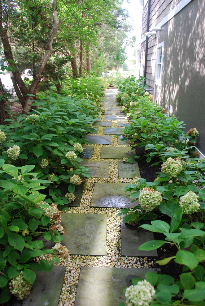 Réalisation d'un aménagement d'entrée ou allée de jardin avant tradition l'été avec une exposition ombragée et des pavés en pierre naturelle.