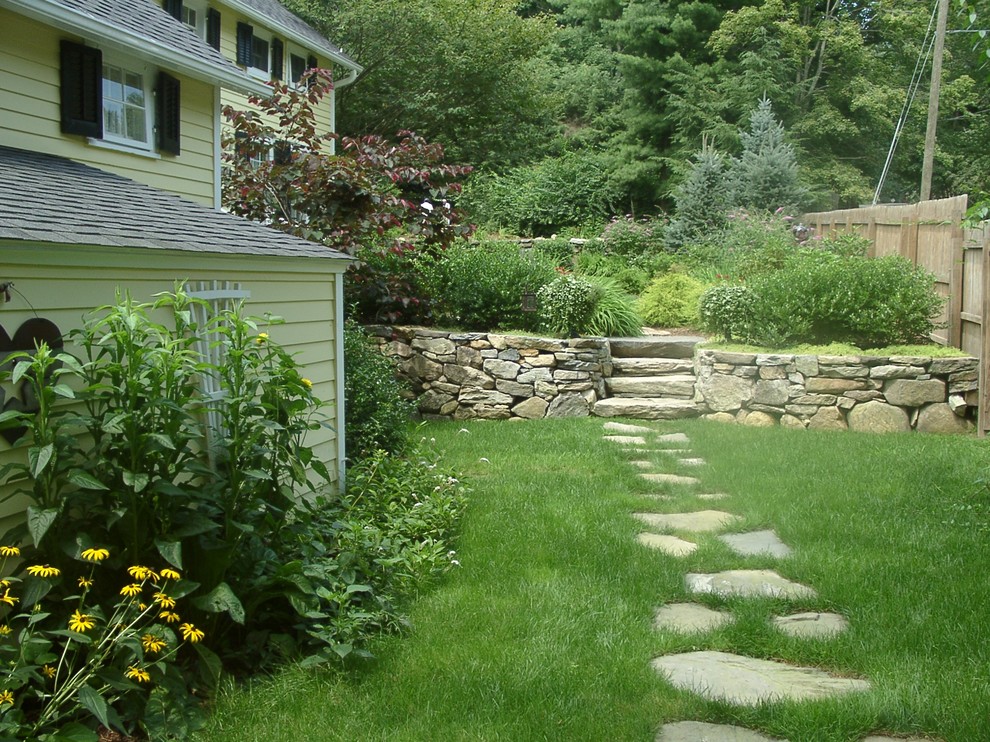 This is an example of a farmhouse front full sun garden for summer in New York with a retaining wall and natural stone paving.