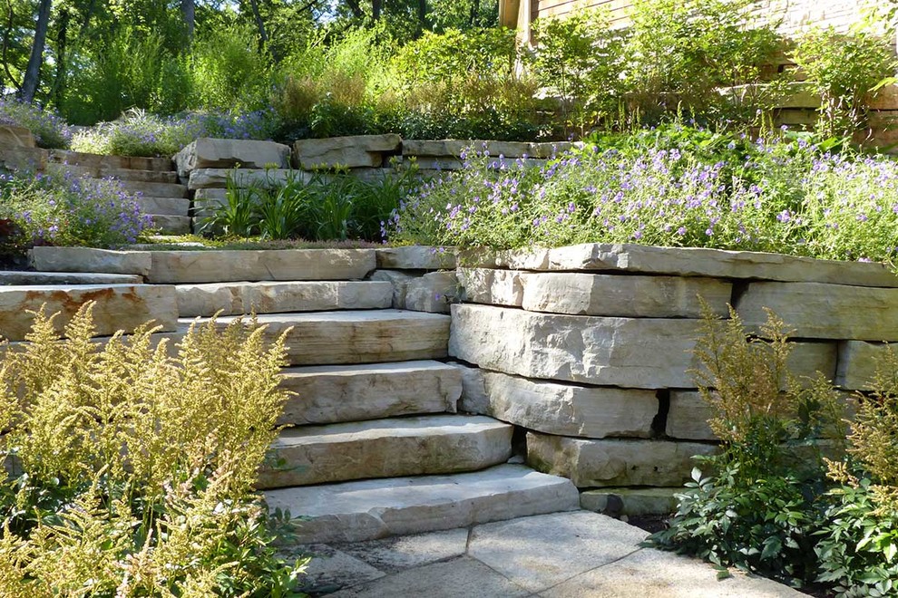 This is an example of a large farmhouse back xeriscape partial sun garden for summer in Chicago with a retaining wall and natural stone paving.