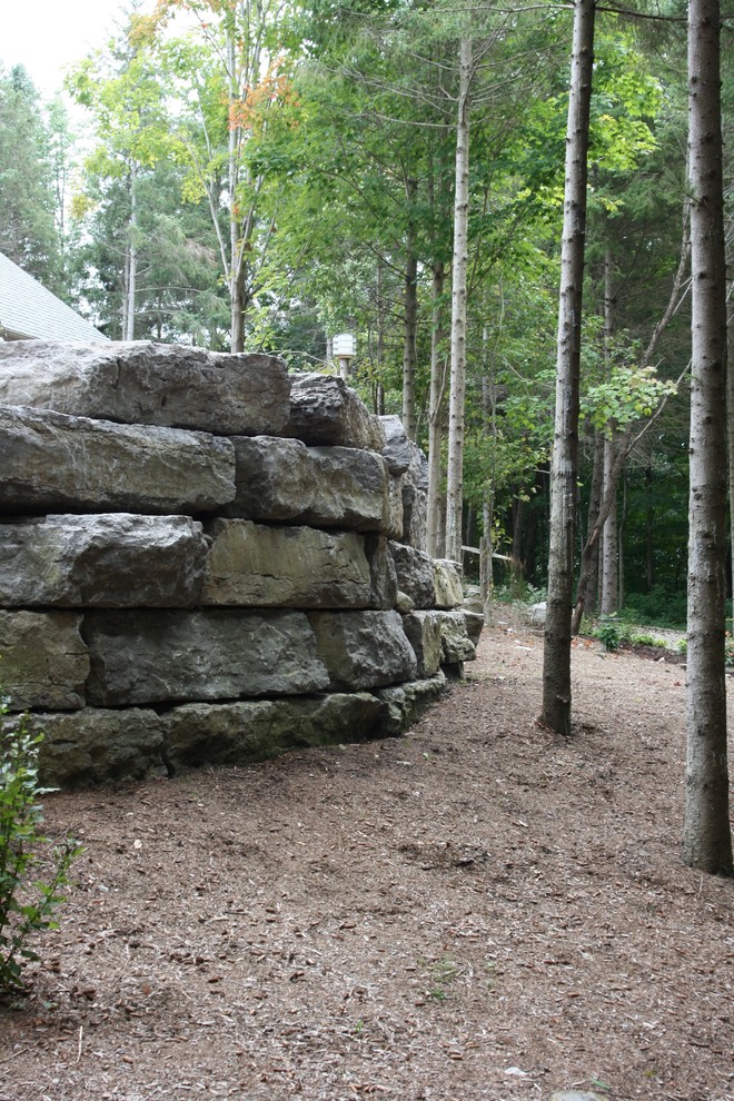 This is an example of a large rustic backyard stone retaining wall landscape in Toronto.
