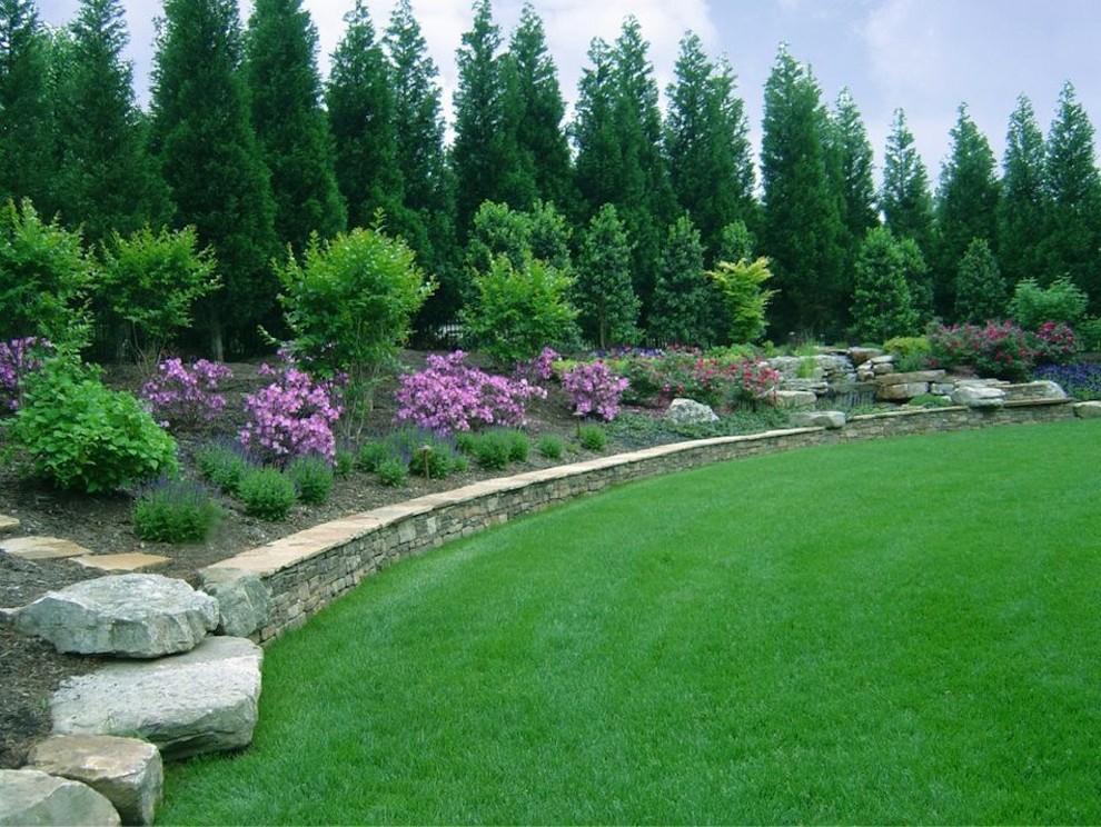 Cette image montre un jardin arrière traditionnel avec un mur de soutènement, des pavés en pierre naturelle et une exposition ensoleillée.