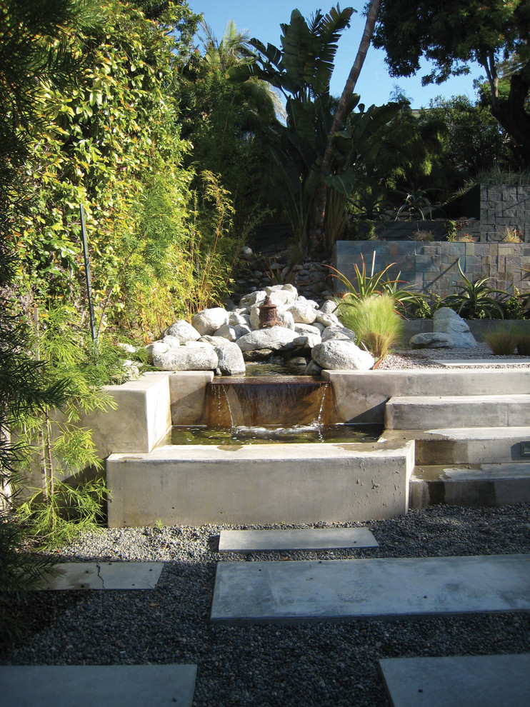Ejemplo de jardín minimalista de tamaño medio en primavera en patio trasero con fuente, exposición parcial al sol y gravilla