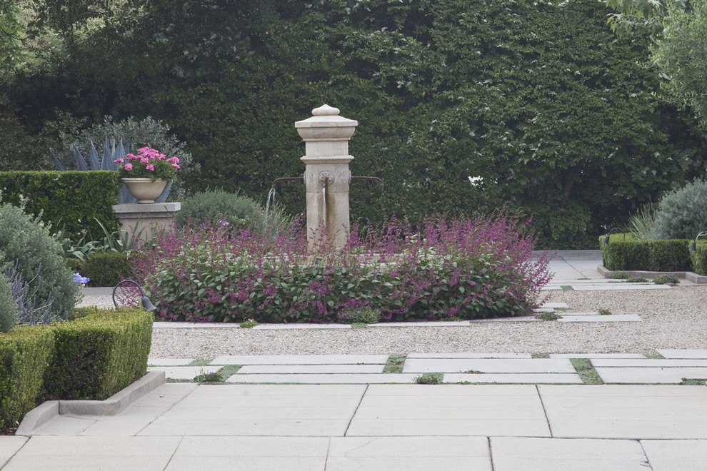 Immagine di un grande giardino formale mediterraneo esposto in pieno sole davanti casa con fontane e pavimentazioni in pietra naturale