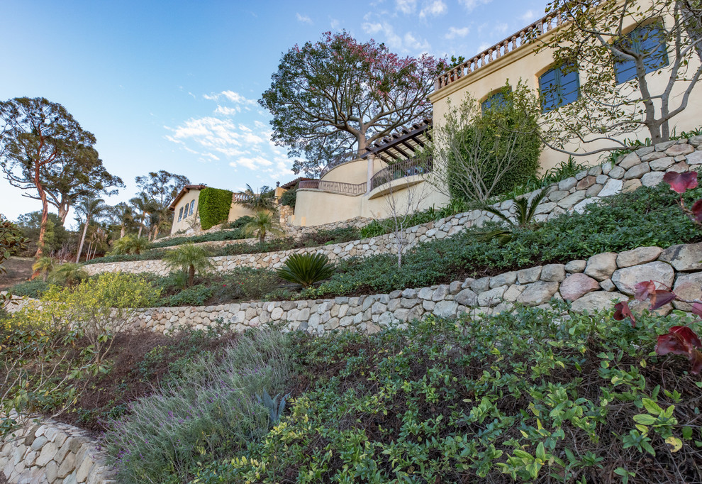 Стильный дизайн: солнечный засухоустойчивый сад на склоне в средиземноморском стиле с подпорной стенкой, хорошей освещенностью и покрытием из каменной брусчатки - последний тренд