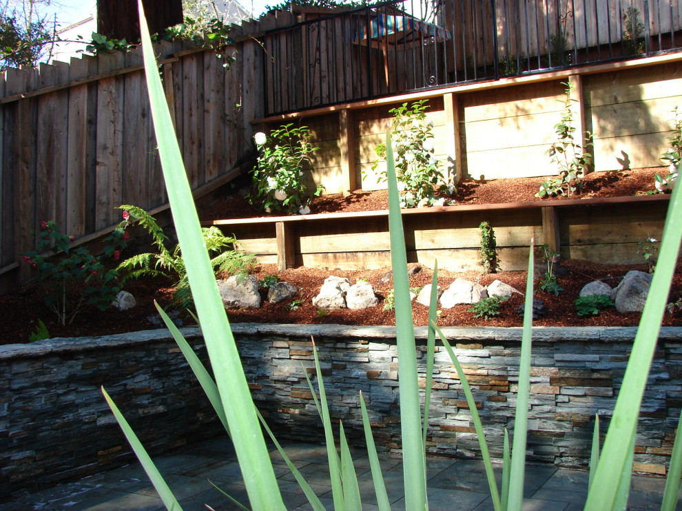 Esempio di un giardino design dietro casa con un muro di contenimento, pavimentazioni in pietra naturale e recinzione in legno
