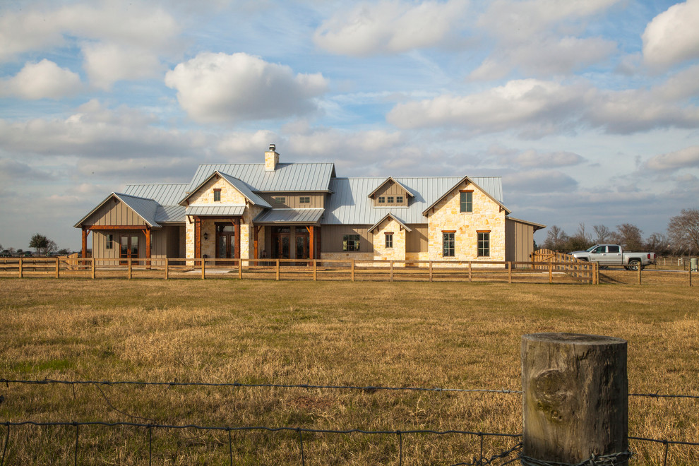 Ejemplo de fachada de casa beige y gris rural grande de dos plantas con revestimiento de piedra, tejado a dos aguas, tejado de metal y panel y listón