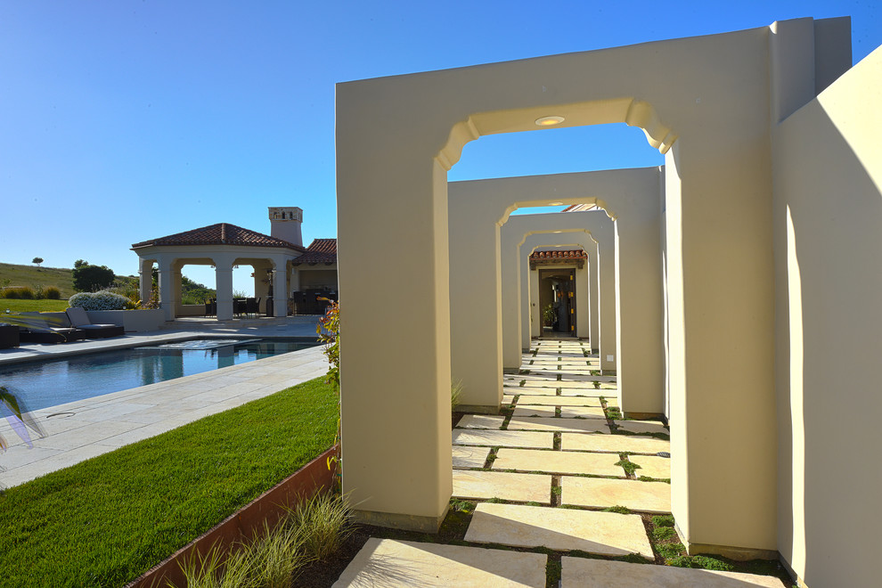 Aménagement d'un grand jardin arrière méditerranéen l'été avec une exposition ensoleillée et des pavés en pierre naturelle.