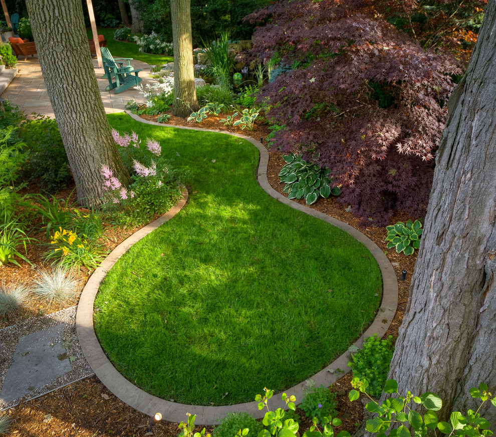 Réalisation d'un grand jardin arrière tradition avec une exposition ombragée, des pavés en pierre naturelle et une bordure.