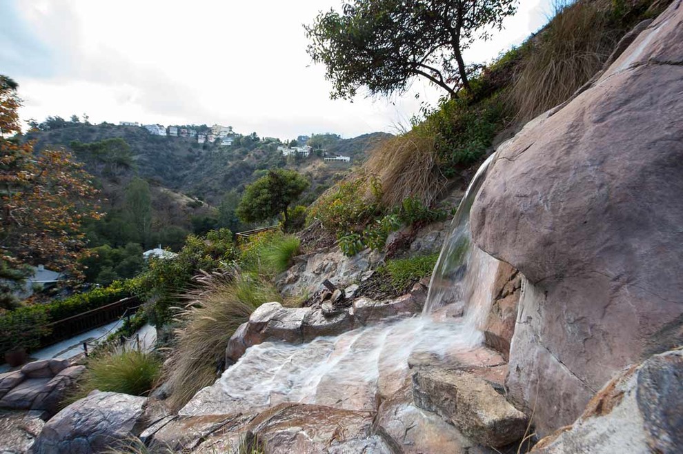 This is an example of a large eclectic full sun hillside stone water fountain landscape in Los Angeles.