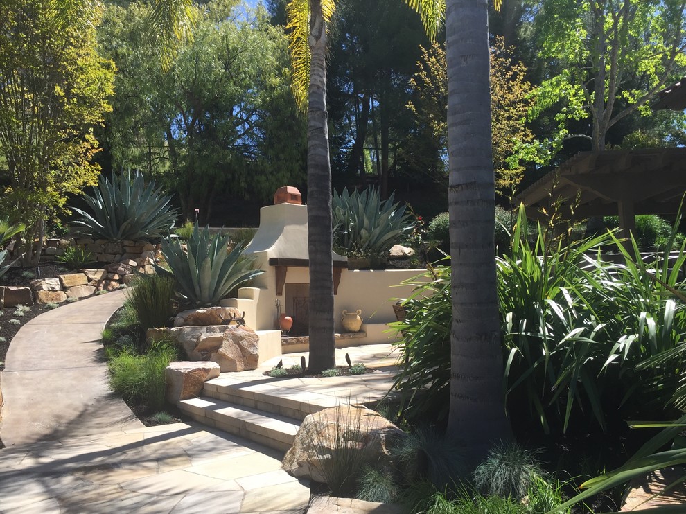 Imagen de jardín mediterráneo grande en verano en patio trasero con exposición total al sol y adoquines de hormigón