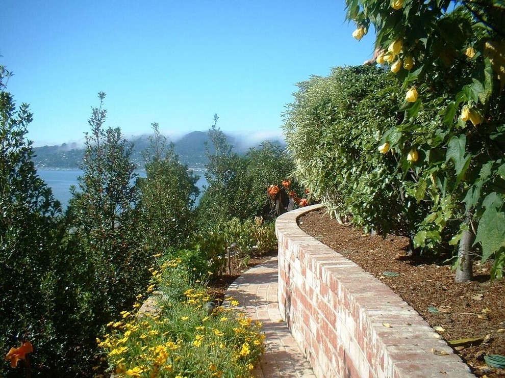 На фото: большой солнечный регулярный сад на склоне в современном стиле с подпорной стенкой, хорошей освещенностью и мощением клинкерной брусчаткой с