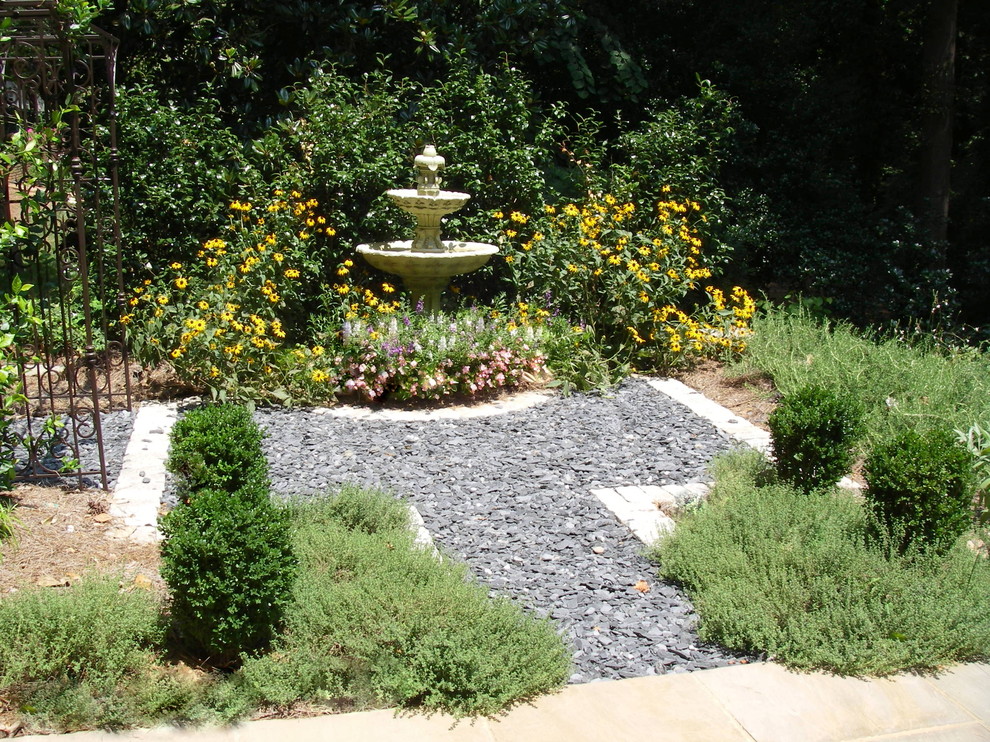 Imagen de jardín tradicional pequeño en verano en patio con jardín francés, fuente, exposición total al sol y gravilla