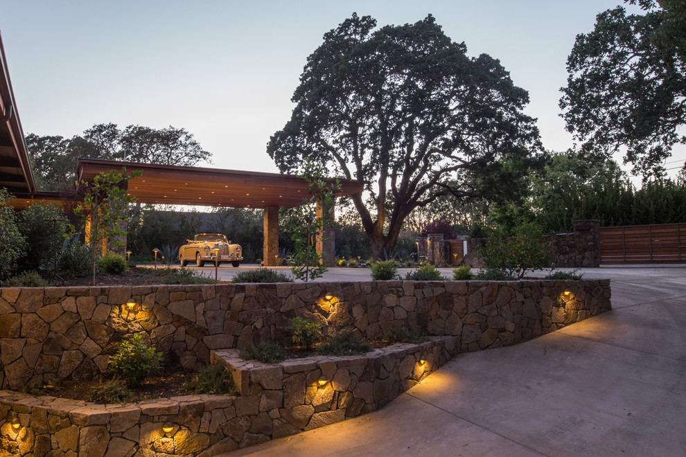 This is an example of a large midcentury front partial sun garden with a retaining wall and natural stone paving.