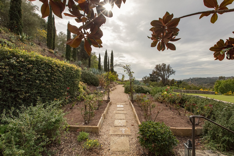 Стильный дизайн: огромный солнечный, весенний регулярный сад на заднем дворе в средиземноморском стиле с садовой дорожкой или калиткой, хорошей освещенностью и покрытием из каменной брусчатки - последний тренд