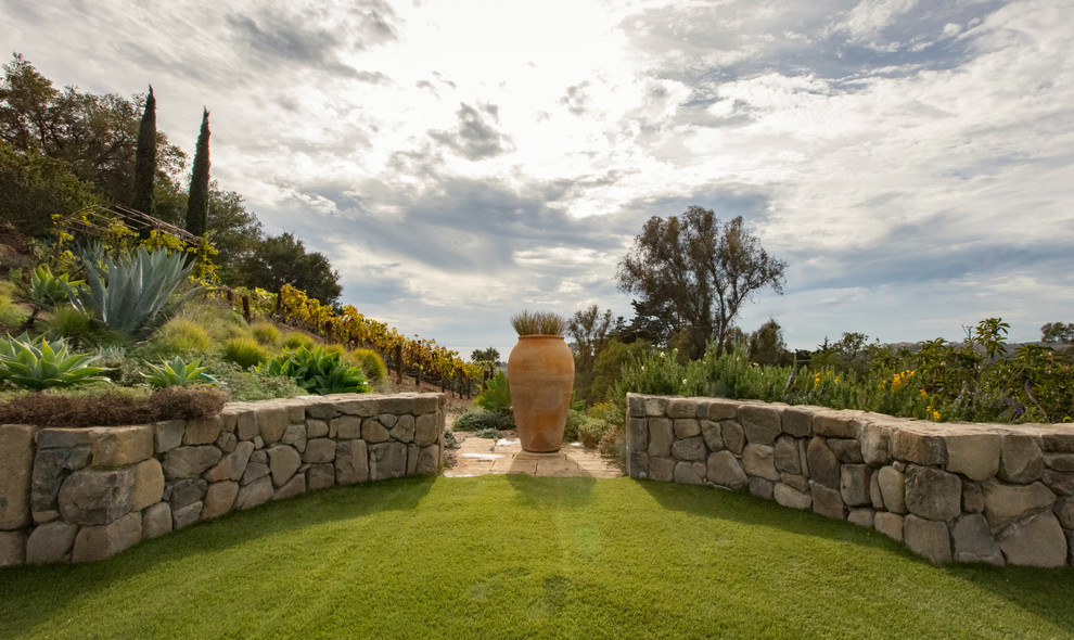 Стильный дизайн: большой солнечный засухоустойчивый сад на заднем дворе в средиземноморском стиле с хорошей освещенностью, покрытием из каменной брусчатки и подпорной стенкой - последний тренд