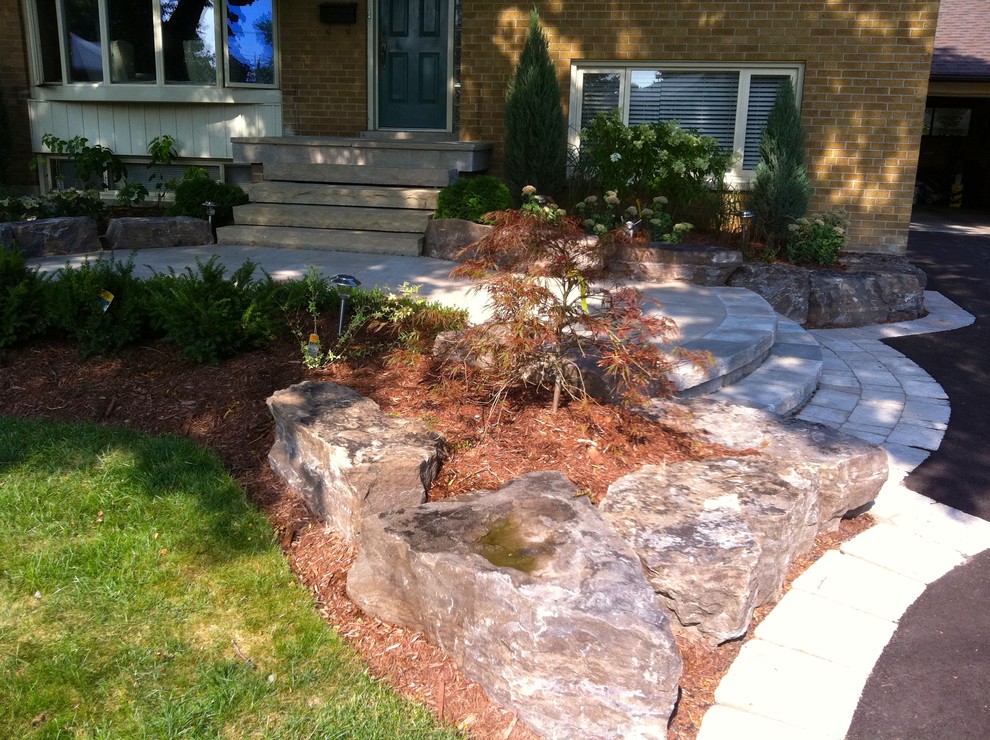 This is an example of a small traditional courtyard driveway fully shaded garden for autumn in Toronto with a retaining wall and natural stone paving.