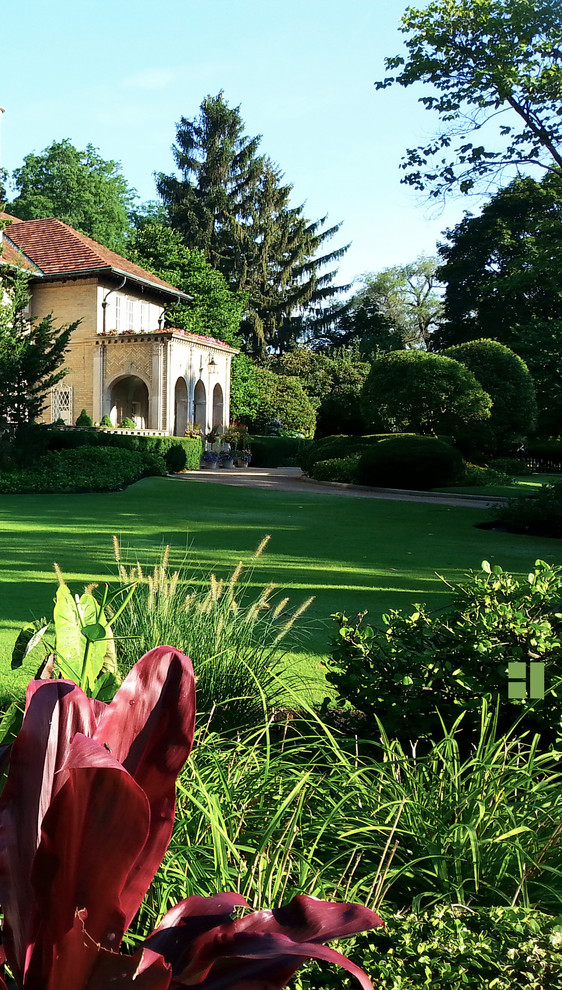 Cette photo montre un grand jardin à la française avant méditerranéen au printemps avec une exposition ensoleillée, un mur de soutènement et des pavés en pierre naturelle.