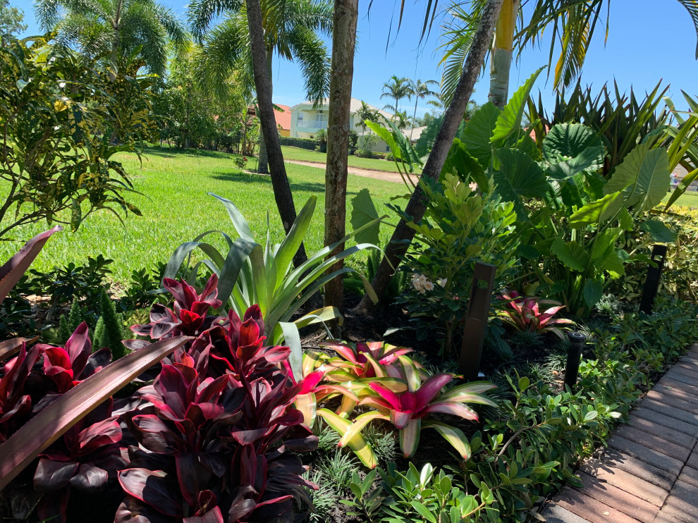 Foto på en liten tropisk bakgård i delvis sol som tål torka, blomsterrabatt och flodsten
