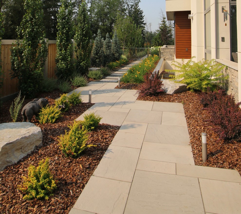 Large contemporary side formal full sun garden for summer in Edmonton with a garden path and concrete paving.
