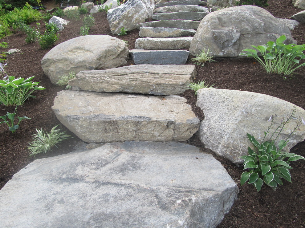 Large rustic sloped partial sun garden for summer in Boston with natural stone paving and a garden path.