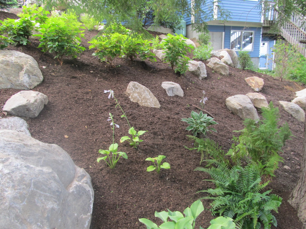 This is an example of a mid-sized rustic partial sun hillside mulch retaining wall landscape in Boston for summer.