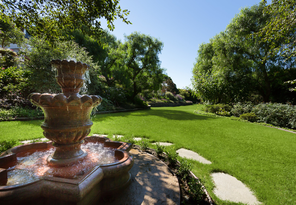 Immagine di un ampio giardino formale tradizionale esposto in pieno sole dietro casa in primavera con fontane e pavimentazioni in pietra naturale
