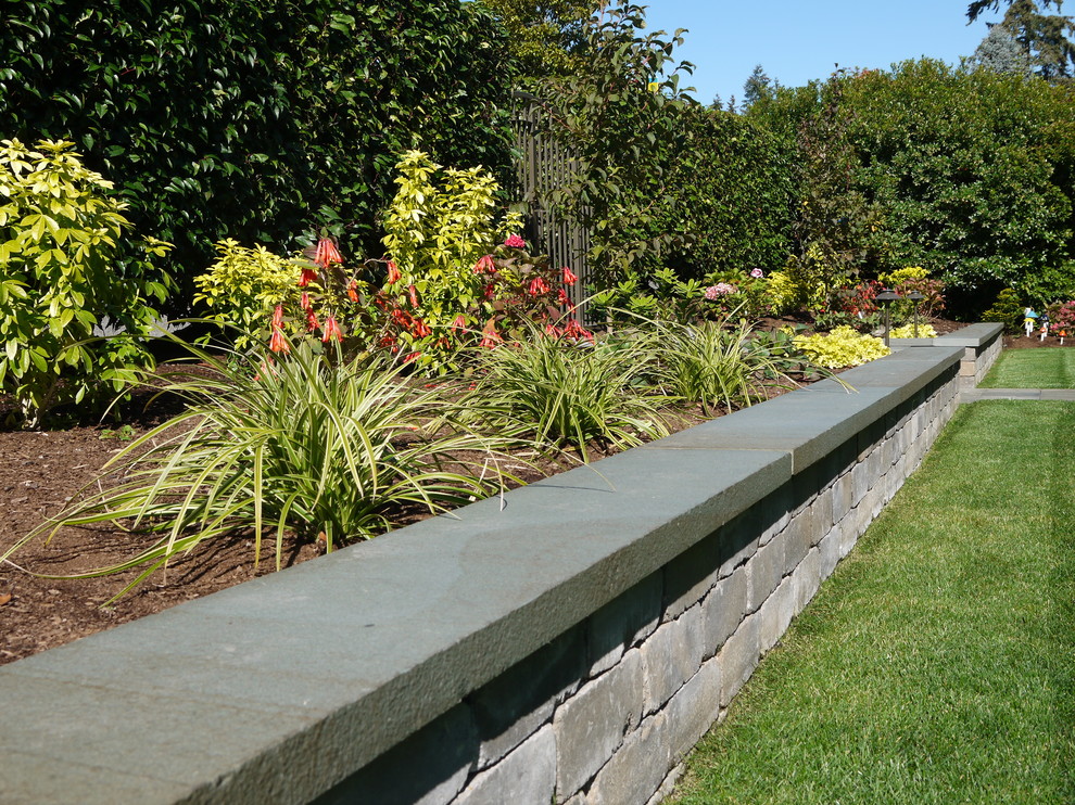 Cette image montre un grand jardin avant minimaliste avec un mur de soutènement, une exposition partiellement ombragée et des pavés en pierre naturelle.
