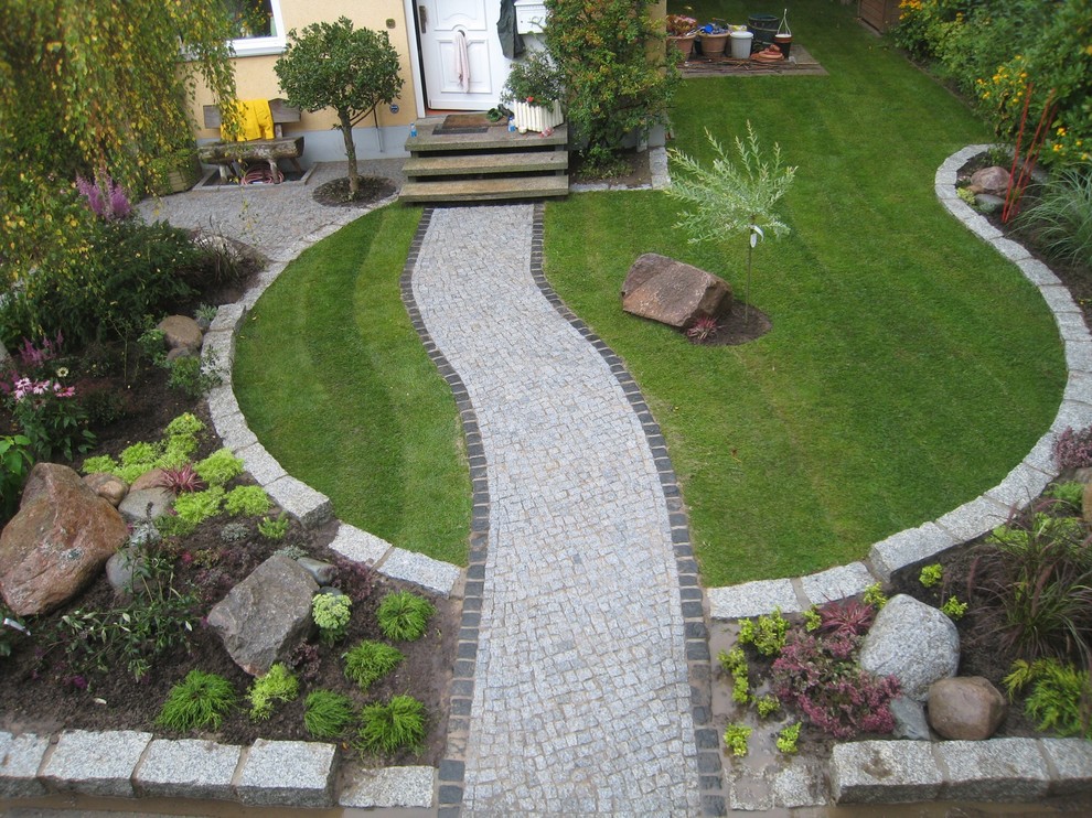 Diseño de jardín actual de tamaño medio en primavera en patio delantero con jardín francés, muro de contención, exposición total al sol y adoquines de ladrillo