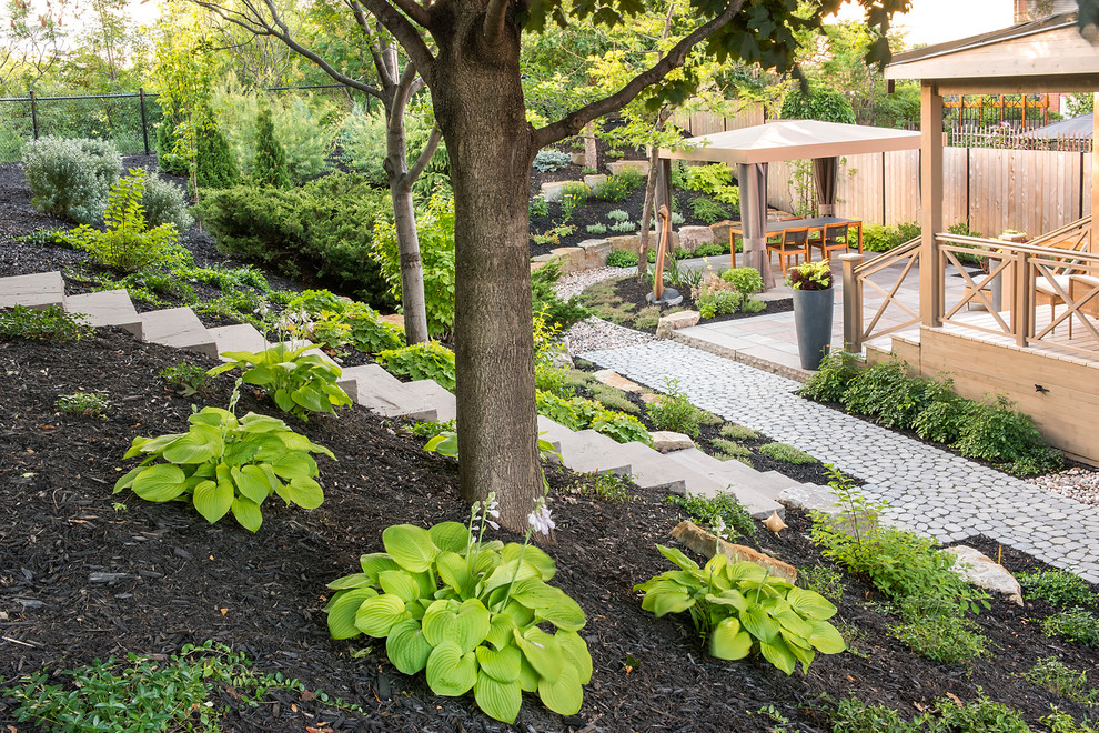 This is an example of a large classic back xeriscape partial sun garden for summer in Montreal with a retaining wall and natural stone paving.