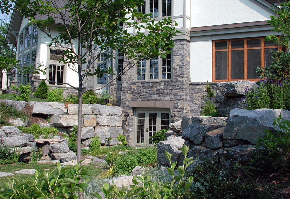 Idée de décoration pour un grand jardin arrière champêtre au printemps avec un mur de soutènement, une exposition ensoleillée et des pavés en pierre naturelle.