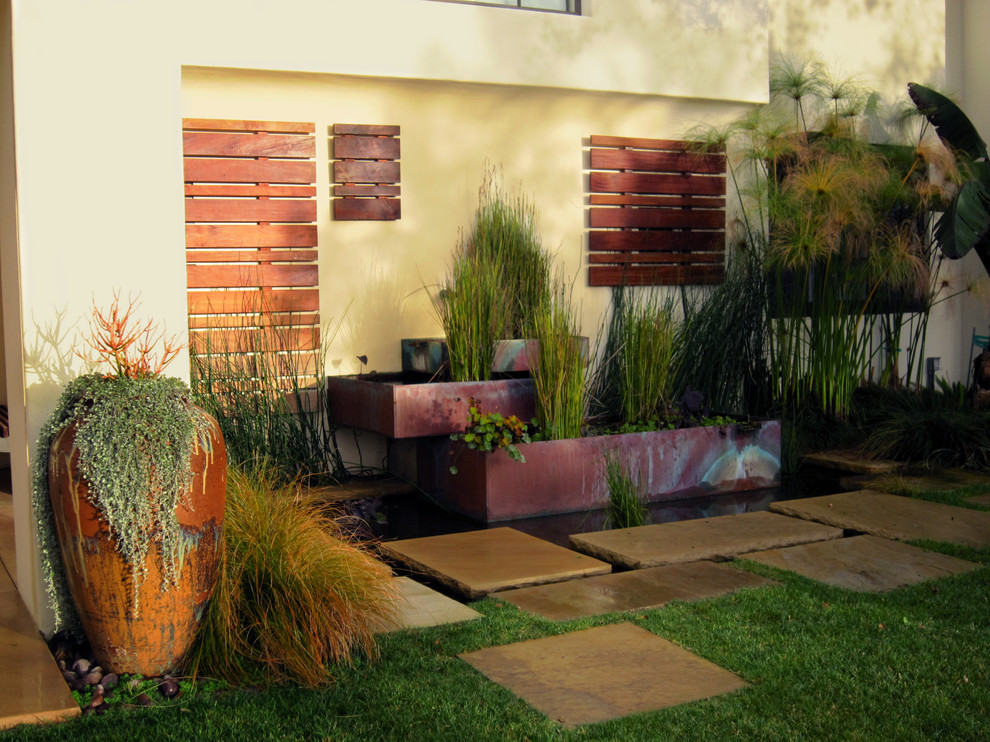 Modelo de jardín de estilo americano de tamaño medio en verano en patio trasero con fuente, exposición parcial al sol, adoquines de piedra natural y jardín francés