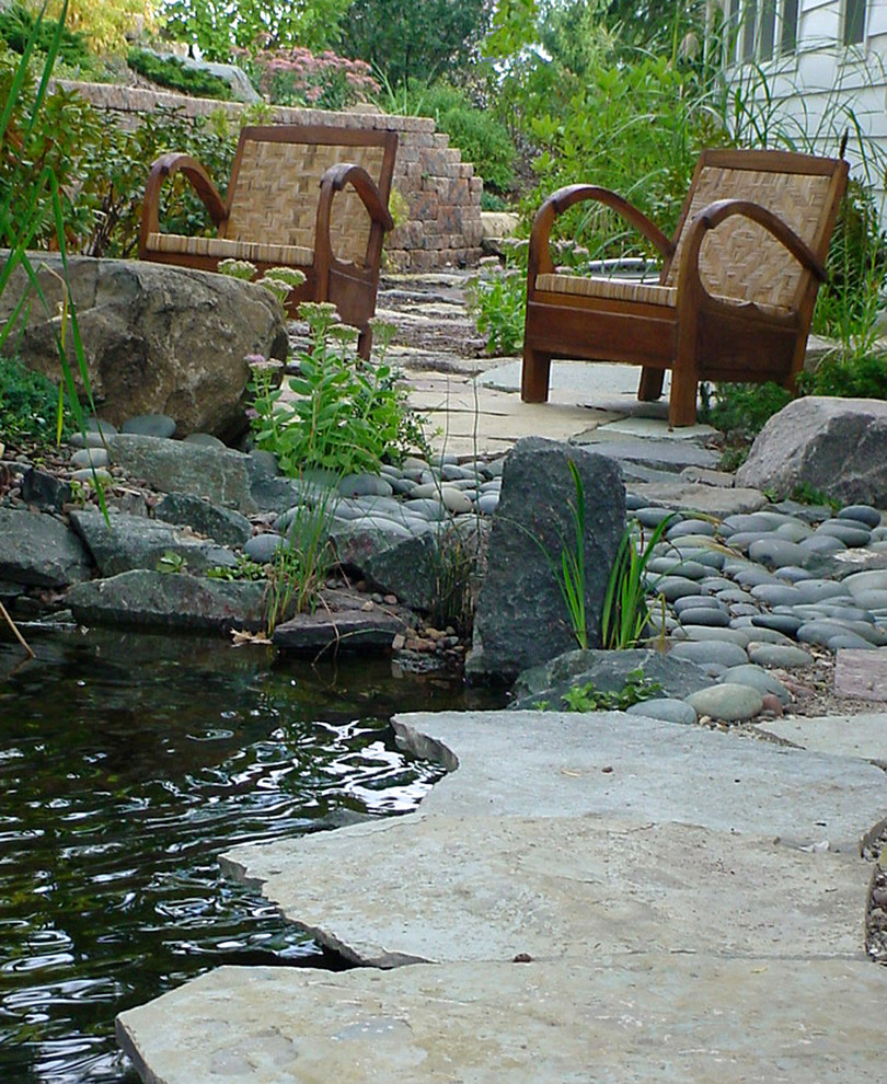 Halbschattiger Asiatischer Gartenteich im Sommer, neben dem Haus mit Natursteinplatten in Milwaukee